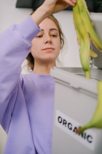 Virtuvėje prie stalviršio matomi keli rūšiavimo konteineriai su užrašais ir aiškia tvarka