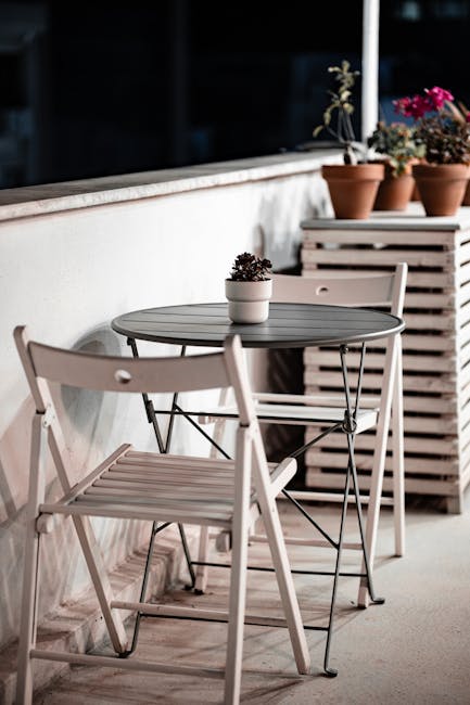 Siauras balkonas su tvarkingai išdėstytais sulankstomais baldais ir saugykla