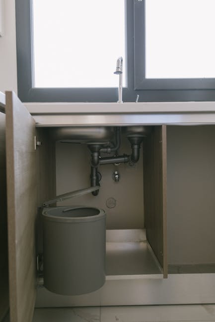 Vandens nuotėkio jutiklis po kriaukle su vandens lašais ant grindų